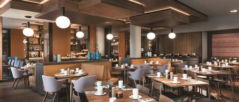 A modern restaurant with wooden tables and chairs, pendant lighting, and a bar area.