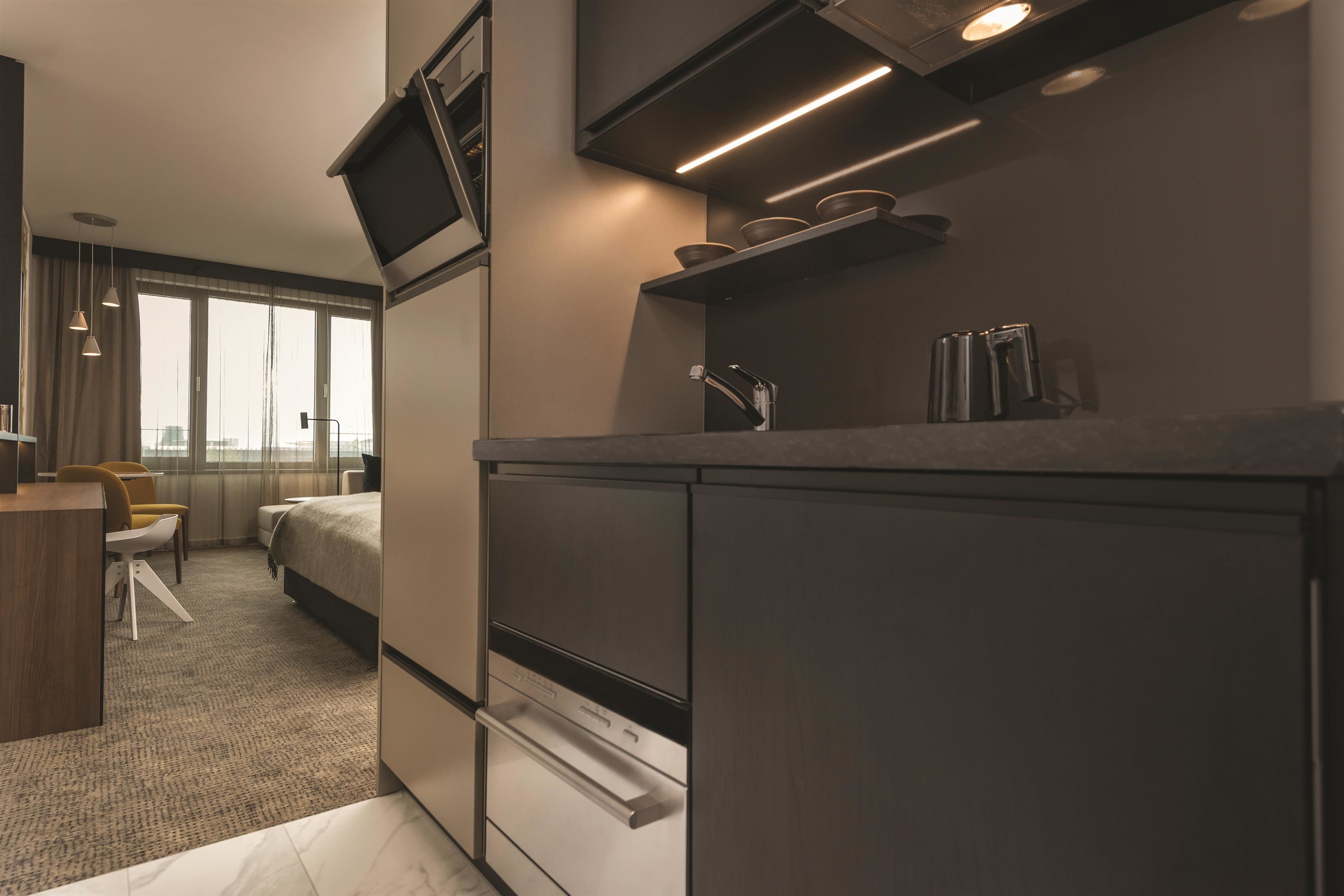 Une chambre d’hôtel moderne équipée d’une kitchenette, d’un lit, d’un bureau et d’une chaise.