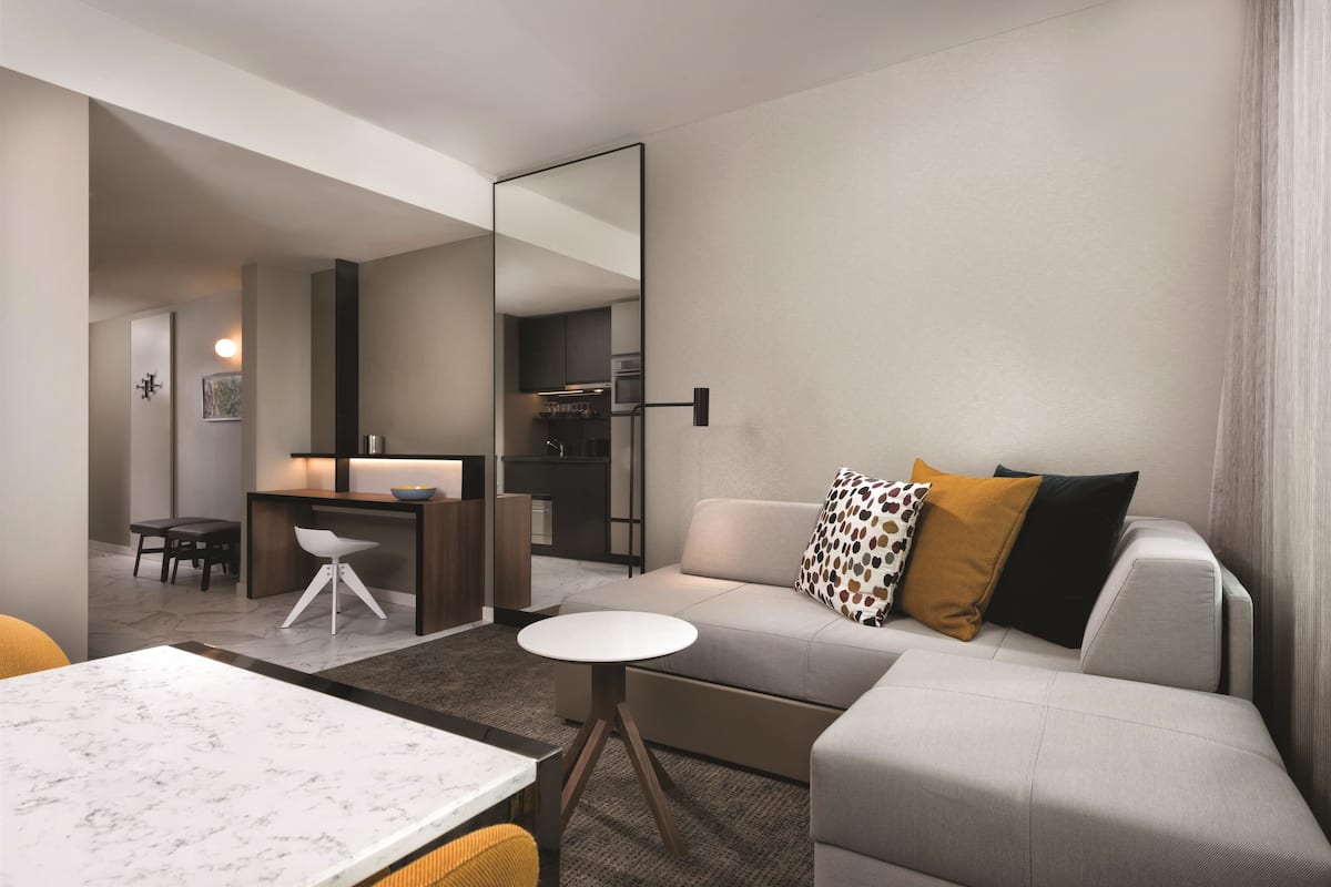 A modern living room with a sofa, a dining table, and a kitchen area visible through an open door.