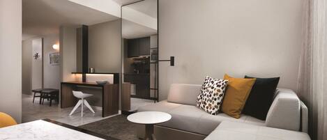 A modern living room with a sofa, a dining table, and a kitchen area visible through an open door.