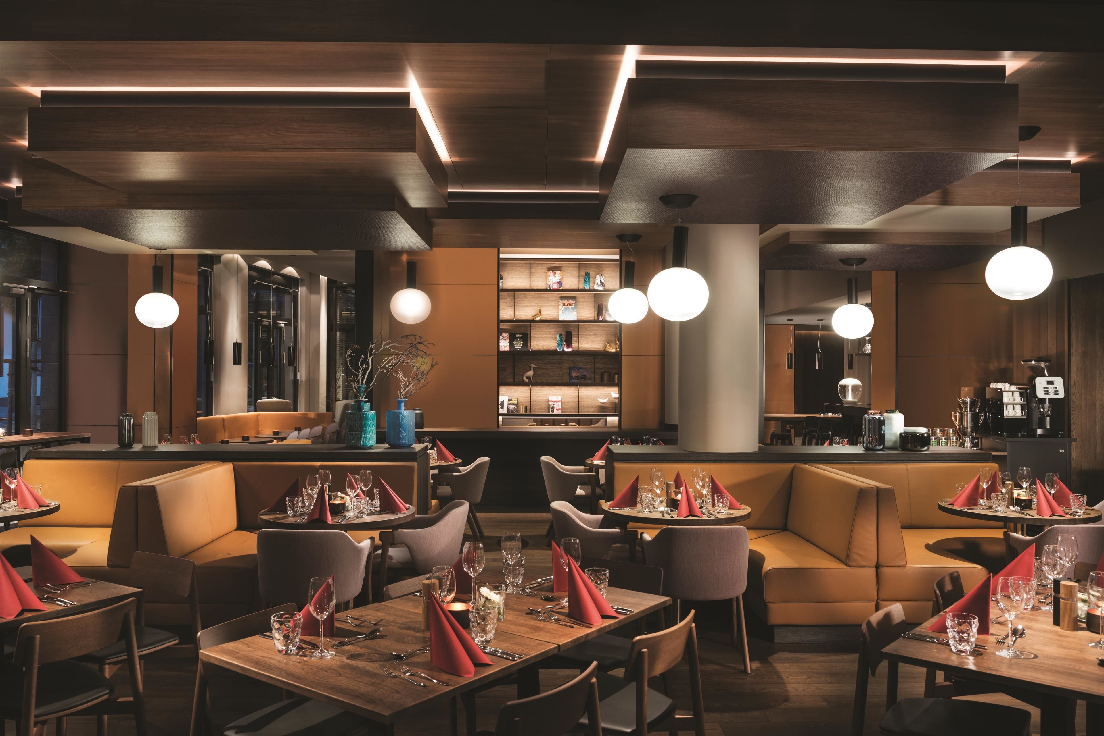 Un restaurant moderne avec des tables et des banquettes en bois, un éclairage d’ambiance et un espace bar.