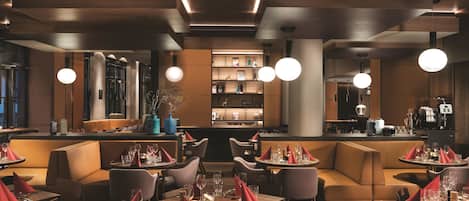 A modern restaurant with wooden tables and booths, ambient lighting, and a bar area.