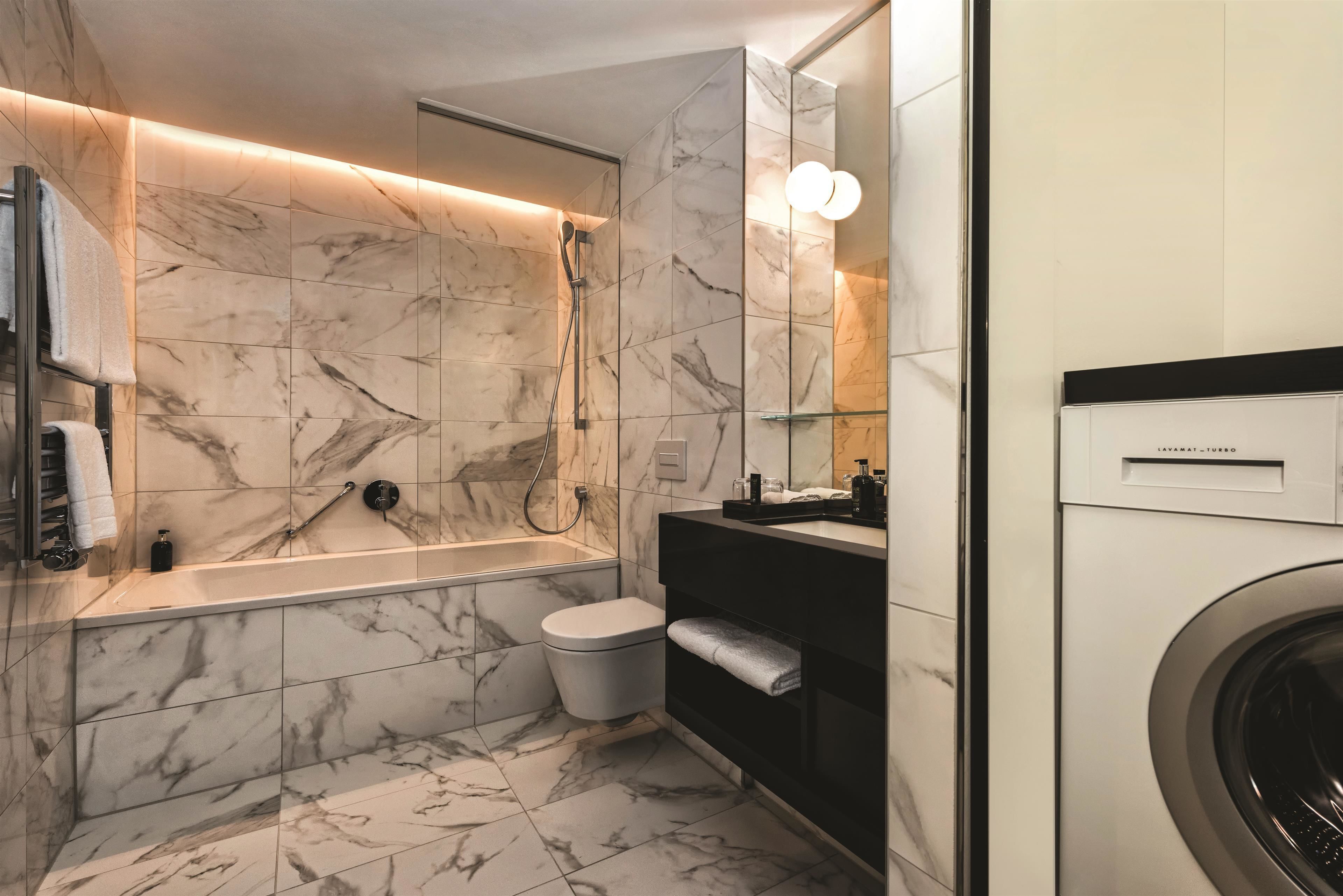 Un baño moderno con suelo de mármol, una bañera, un inodoro, un lavabo y una lavadora.