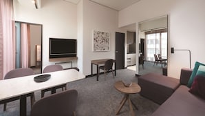 Een moderne hotelkamer met een zithoek, een bank, een televisie en een schilderij aan de muur.