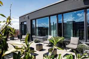 Un edificio moderno con amplias ventanas, asientos exteriores y plantas en macetas.