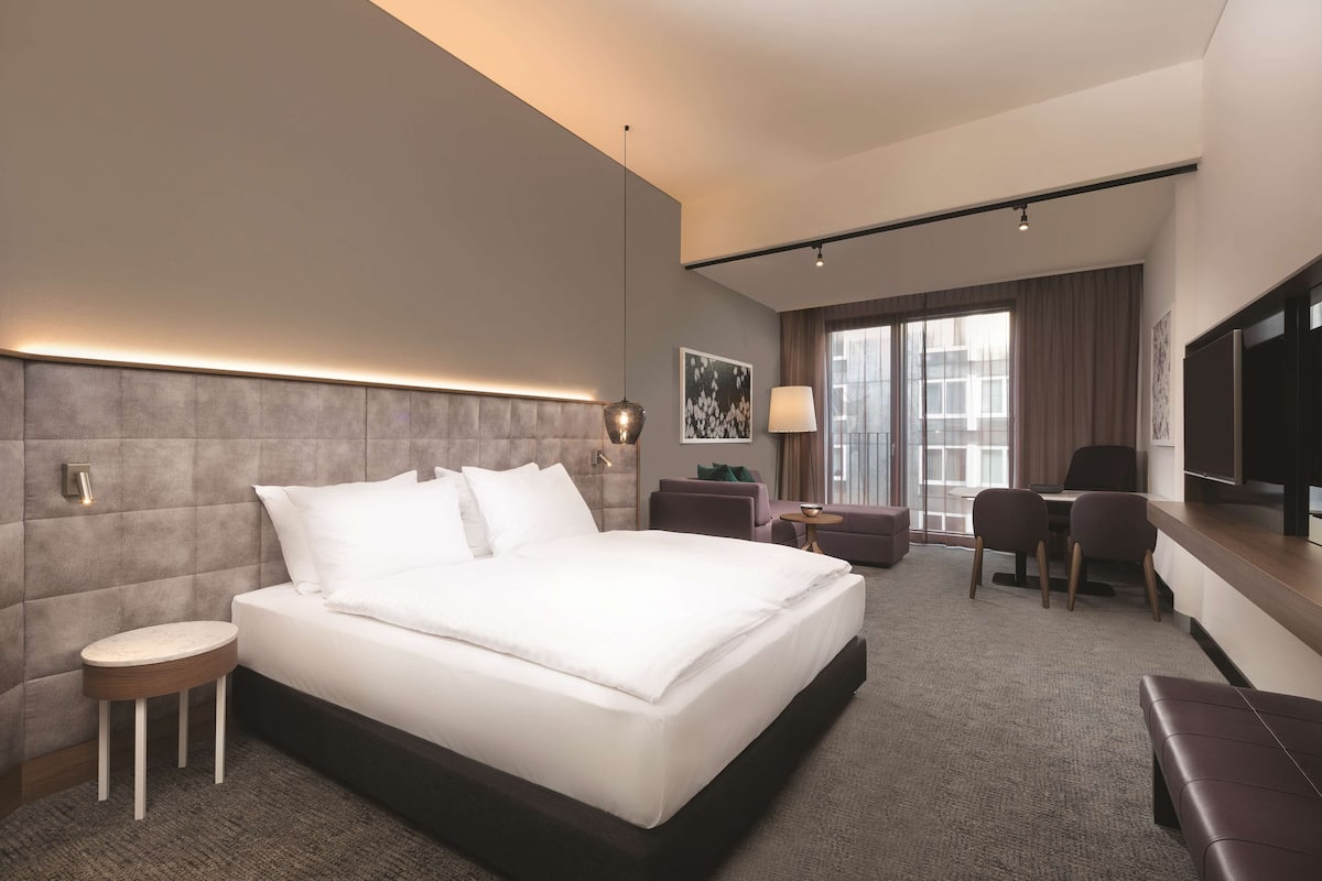 Une chambre d’hôtel moderne avec un grand lit, une petite table de chevet, un bureau avec deux chaises et un téléviseur.