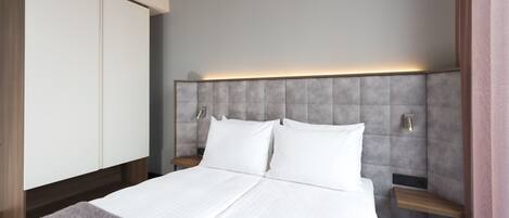 Una habitación de hotel moderna con una cama grande, un armario y un cabecero con iluminación integrada.
