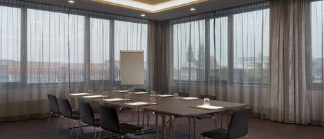 A conference room with a long table, chairs, a whiteboard, and large windows with curtains.
