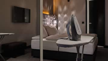 A modern bedroom with a bed, a flat-screen TV mounted on the wall, and an iron on a small table.