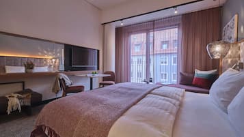 Una camera d'albergo con un letto, una scrivania con televisore, una sedia e una finestra con tende.