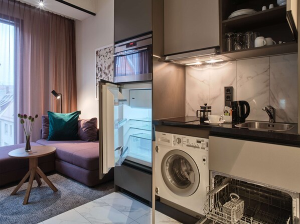 Una cocina compacta con lavadora y secadora integradas, un rincón comedor con una mesita y sofá, y una ventana con cortinas.