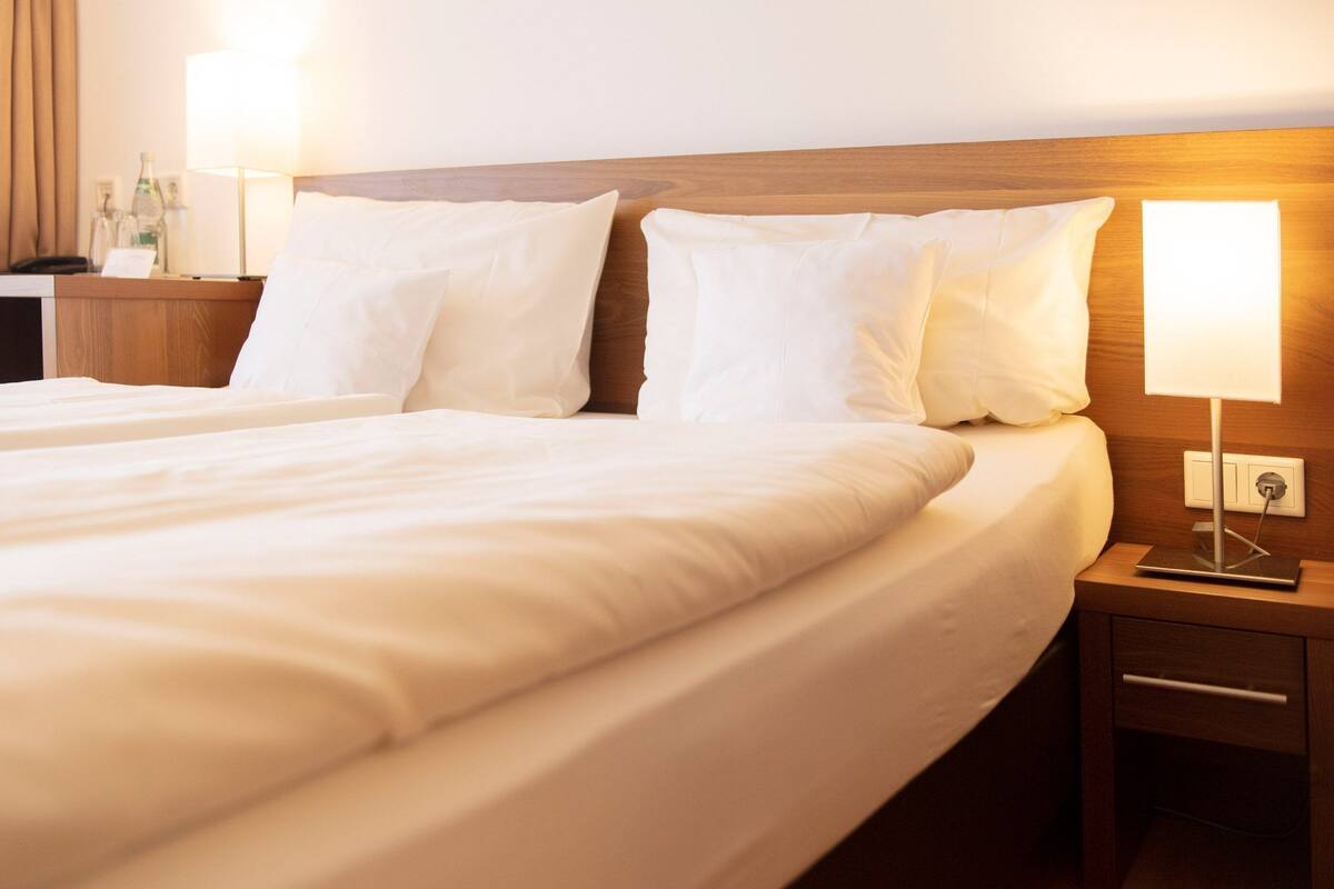 Een hotelkamer met twee bedden, een nachtkastje met een lamp, een stoel en een bureau met een telefoon en een fles.
