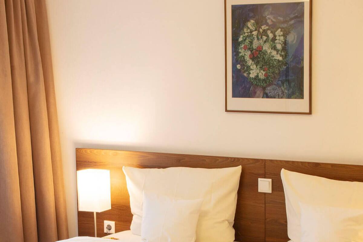 Een tweepersoonsbed met witte lakens, een houten hoofdbord, een bedlampje en een ingelijste schildering aan de muur.