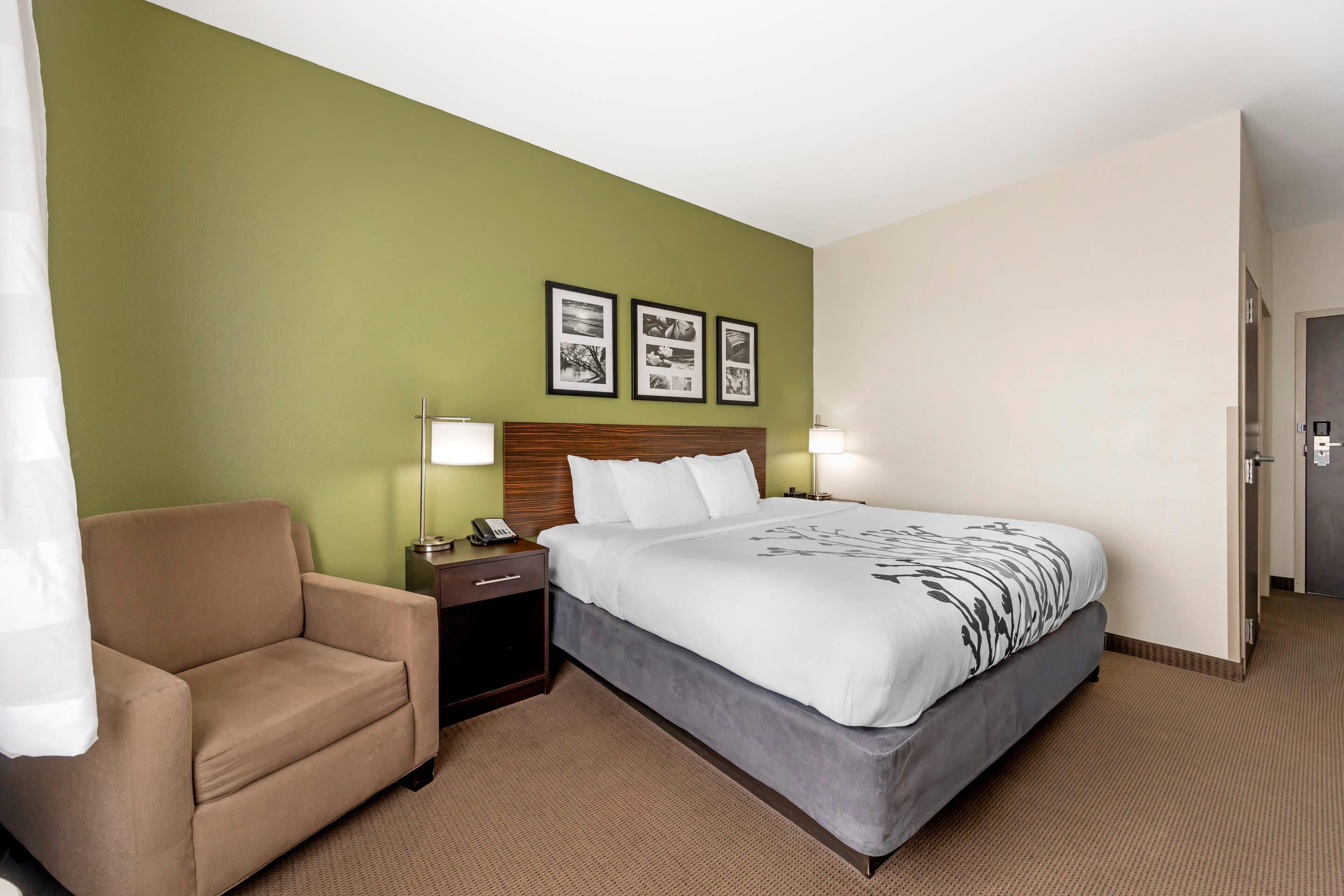 Una habitación de hotel con cama, una silla, una mesita de noche y decoración en la pared.