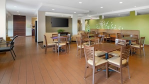 Un grand espace de salle à manger avec plusieurs tables et chaises, un téléviseur à écran plat fixé au mur et un mur d’accent de couleur verte.