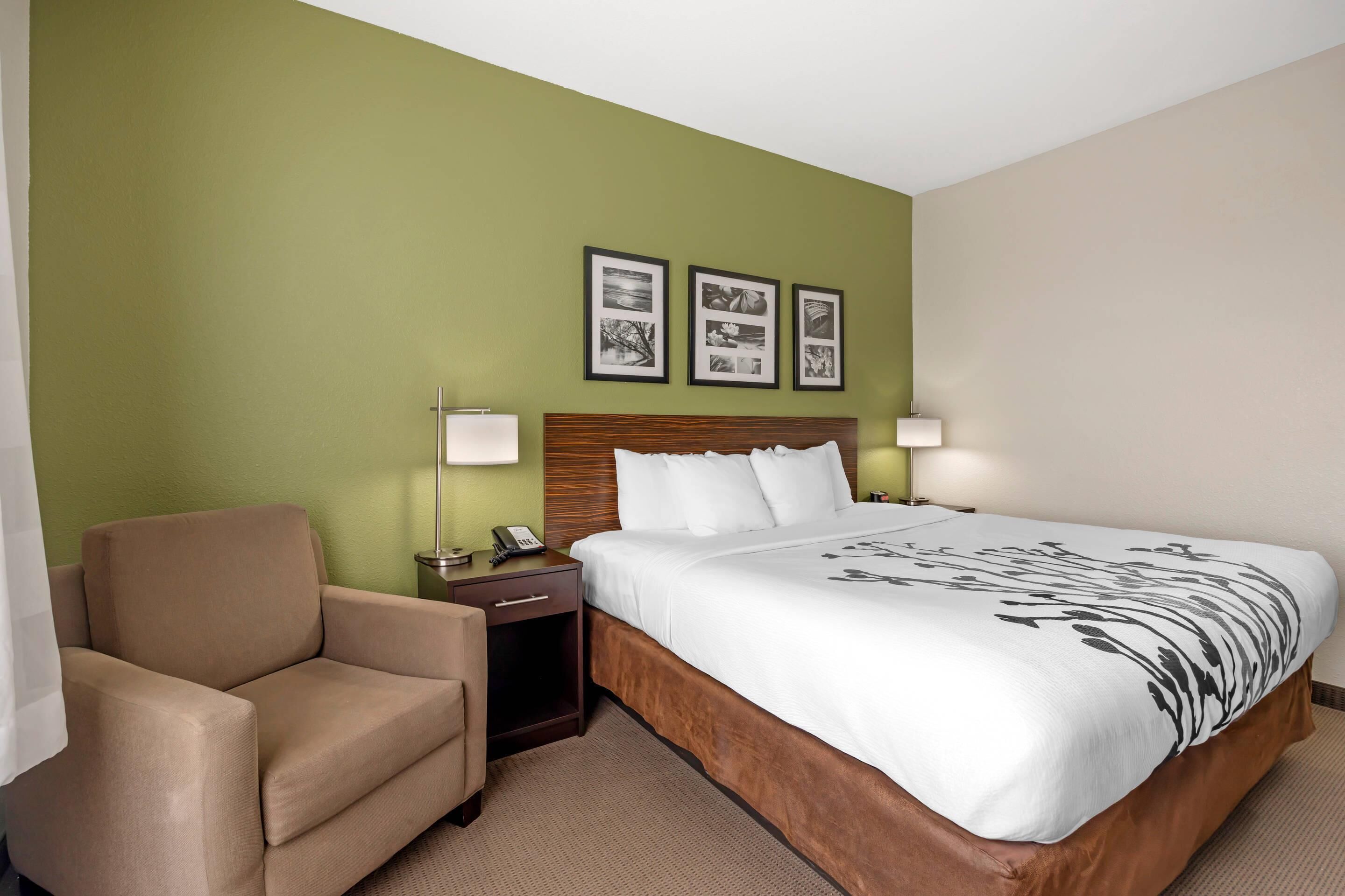 Una habitación de hotel con una cama, una silla, una mesita de noche y dos lámparas fijadas a la pared.