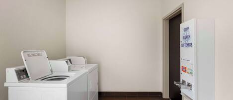 Une buanderie équipée d’un lave-linge, d’un sèche-linge et d’un distributeur mural contenant du savon, de l’eau de Javel et de l’adoucissant.