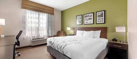 Una habitación de hotel con cama, escritorio, silla, lámpara y pared con tres cuadros enmarcados.