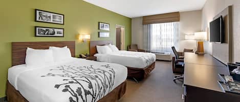 A hotel room with two beds, a desk, a chair, a TV, and framed pictures on the wall.