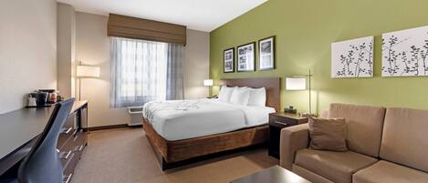 A hotel room with a bed, a desk, a sofa, and a window with curtains.