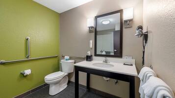 A bathroom with a toilet, sink, mirror, towel rack, and handrails.