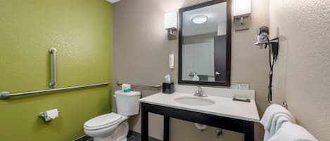 A bathroom with a toilet, sink, mirror, towel rack, and handrails.