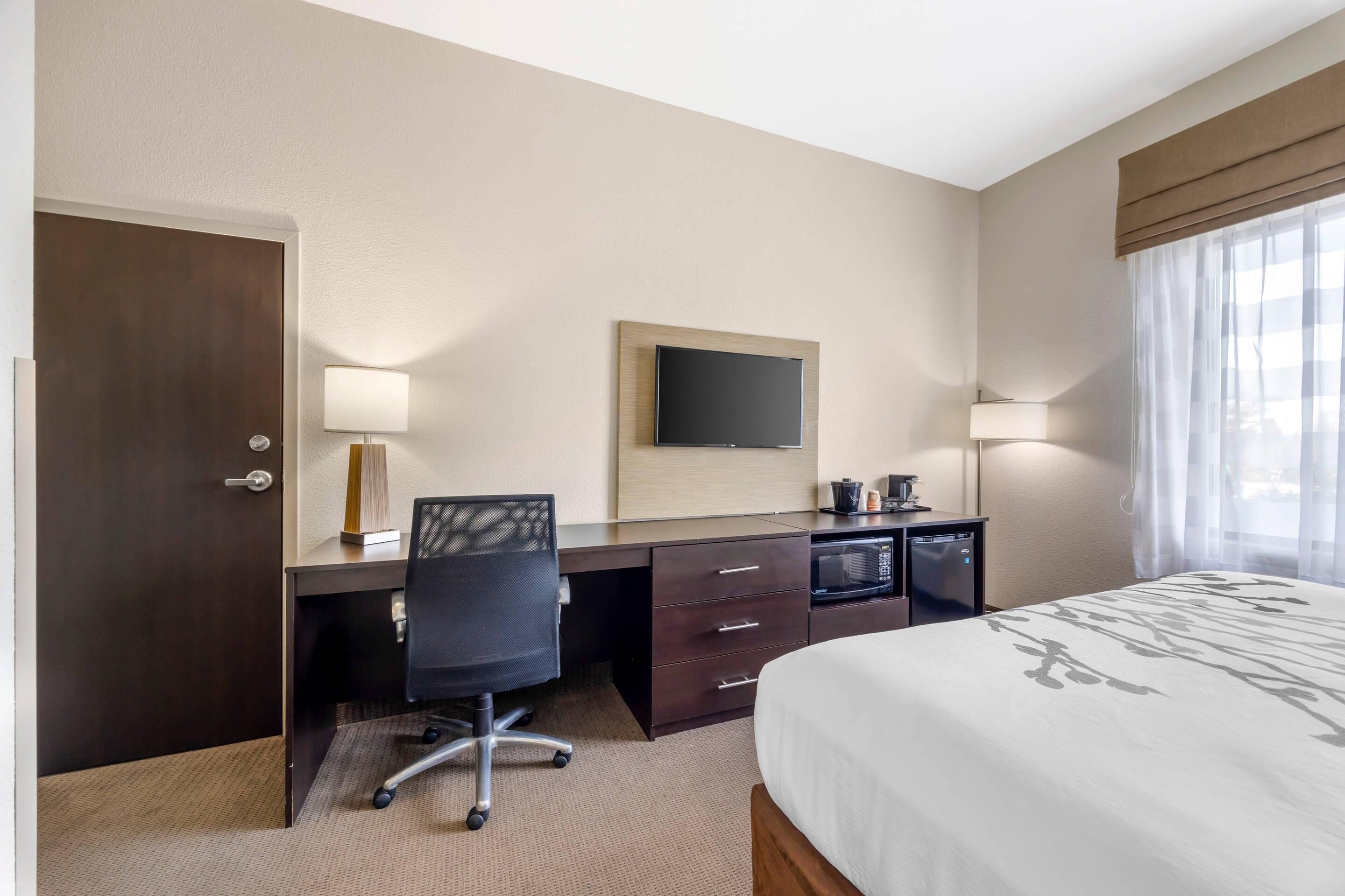 Et hotelværelse med seng, skrivebord med stol, fjernsyn og minibar.