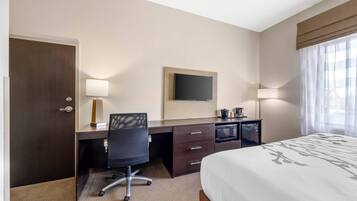 A hotel room with a bed, a desk with a chair, a television, and a minibar.