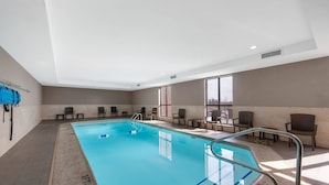 Une piscine intérieure à l’eau d’un bleu cristallin, entourée de chaises et donnant sur une pièce lumineuse aux grandes fenêtres.