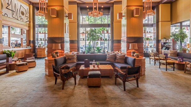 A spacious lobby with a large seating area, wooden accents, and large windows allowing natural light. - Freehand Los Angeles (Los Angeles)