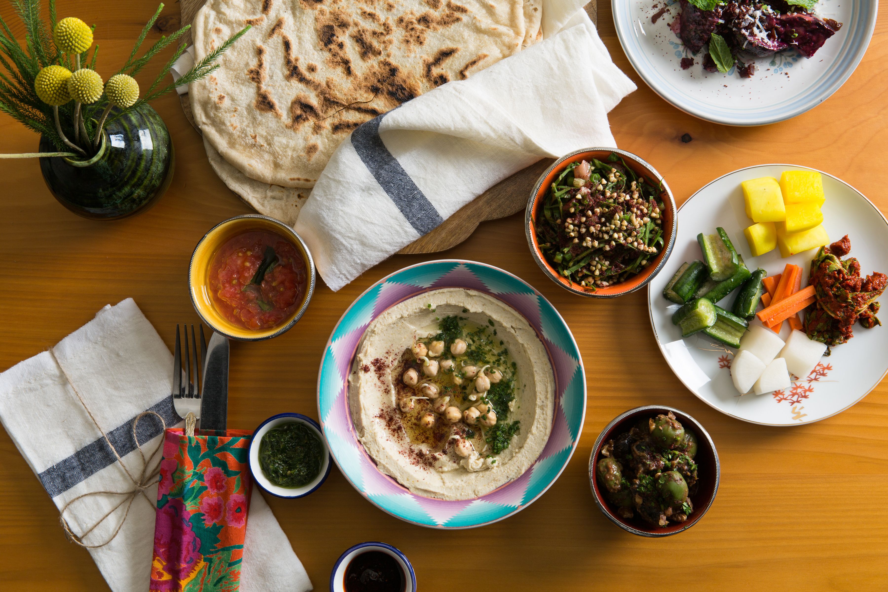 Ein Tisch mit verschiedenen Speisen, darunter ein Hummus-Schälchen, Fladenbrot und eine Platte mit Gemüse und Käse.