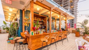 An outdoor bar area with wooden bar counter, stools, and potted plants. - Freehand Los Angeles (Los Angeles)