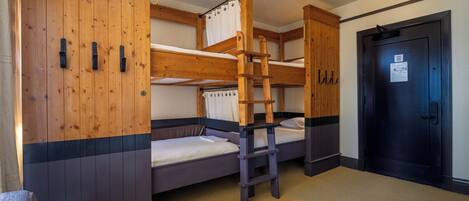Een slaapkamer met een stapelbed, een houten kledingkast en een deur.