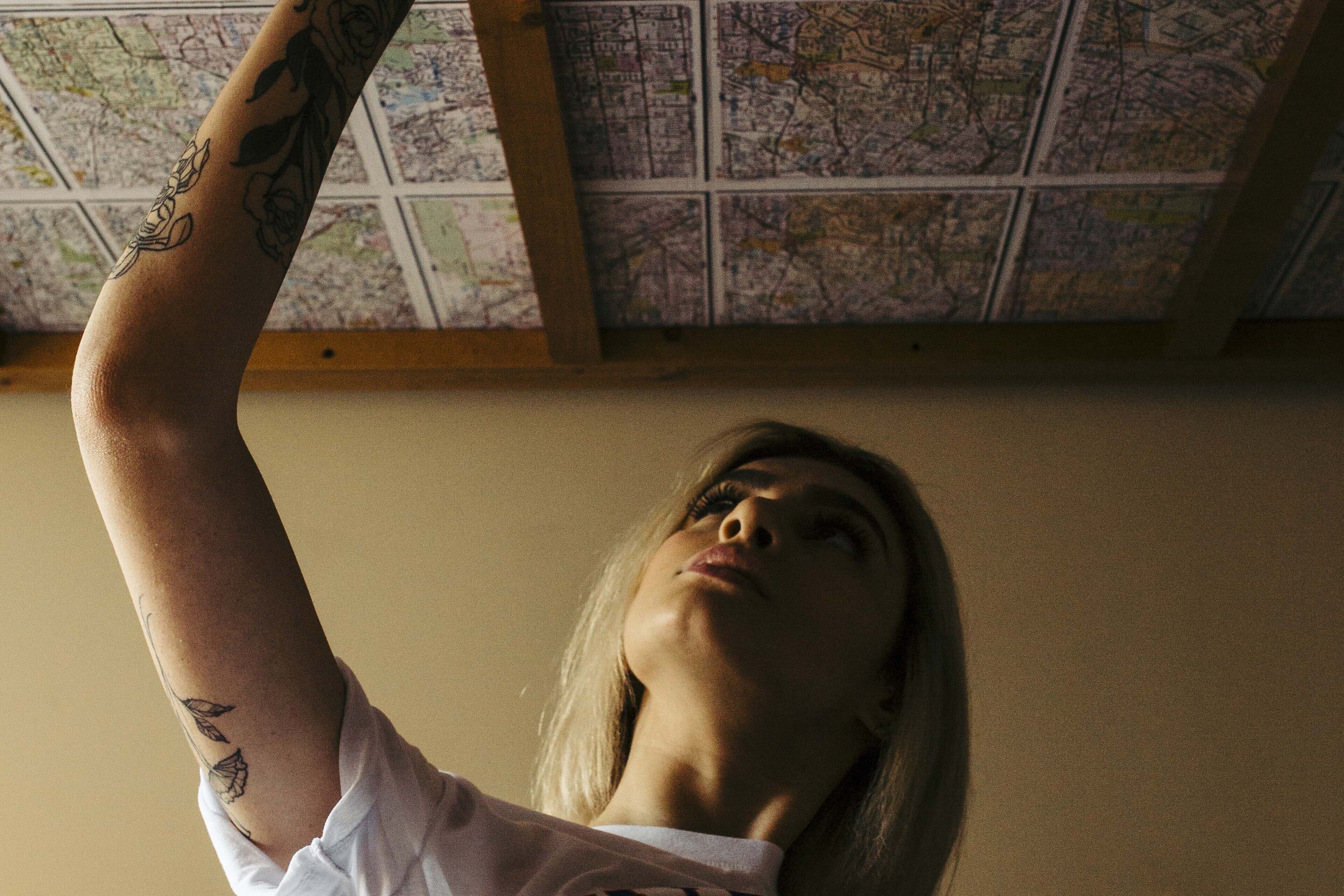 Une personne avec des tatouages sur le bras, debout devant un mur sur lequel est affichée une carte.