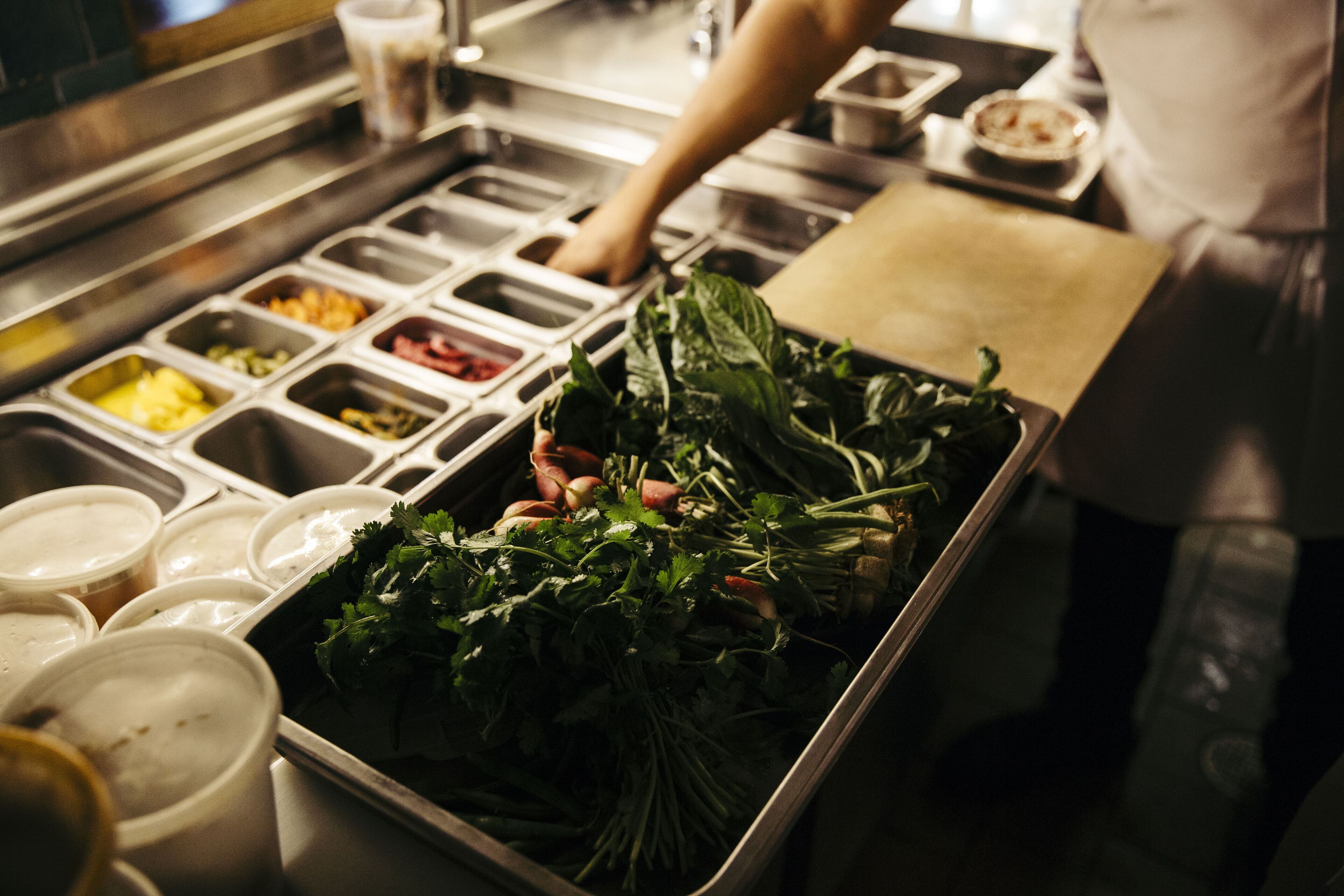A kitchen counter with various food containers and fresh greens.