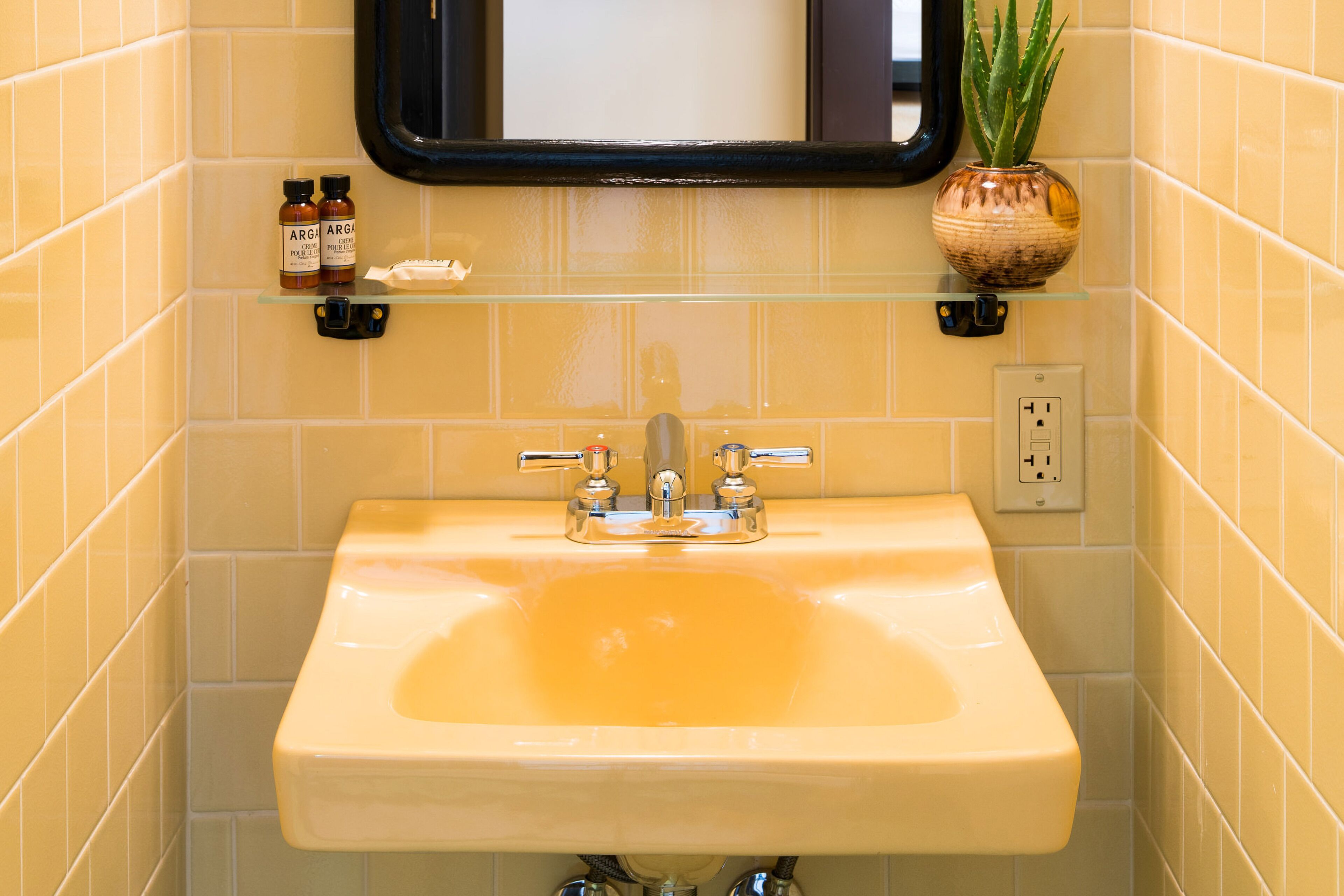 Un baño con un lavamanos amarillo, un espejo y una planta en maceta.