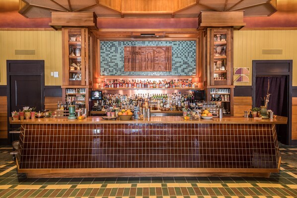 Una zona de bar con un rebozo de azulejos, armarios de madera y una variedad de botellas y vasos sobre la barra.