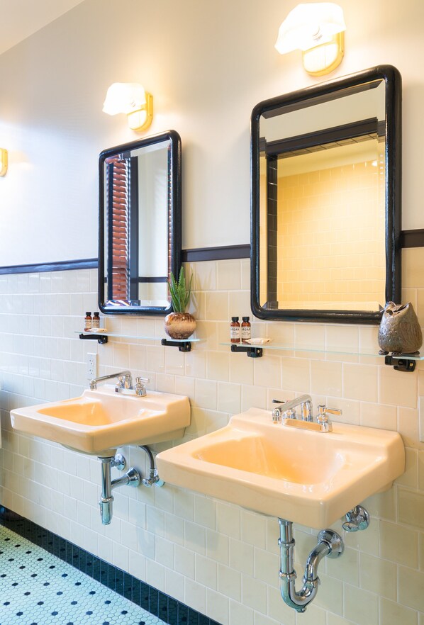 A bathroom with two sinks, a mirror, and wall-mounted shelves with toiletries. - Freehand Los Angeles (Los Angeles)