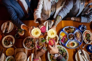 Un grupo de personas brindando con bebidas en una mesa llena de diversos platos.