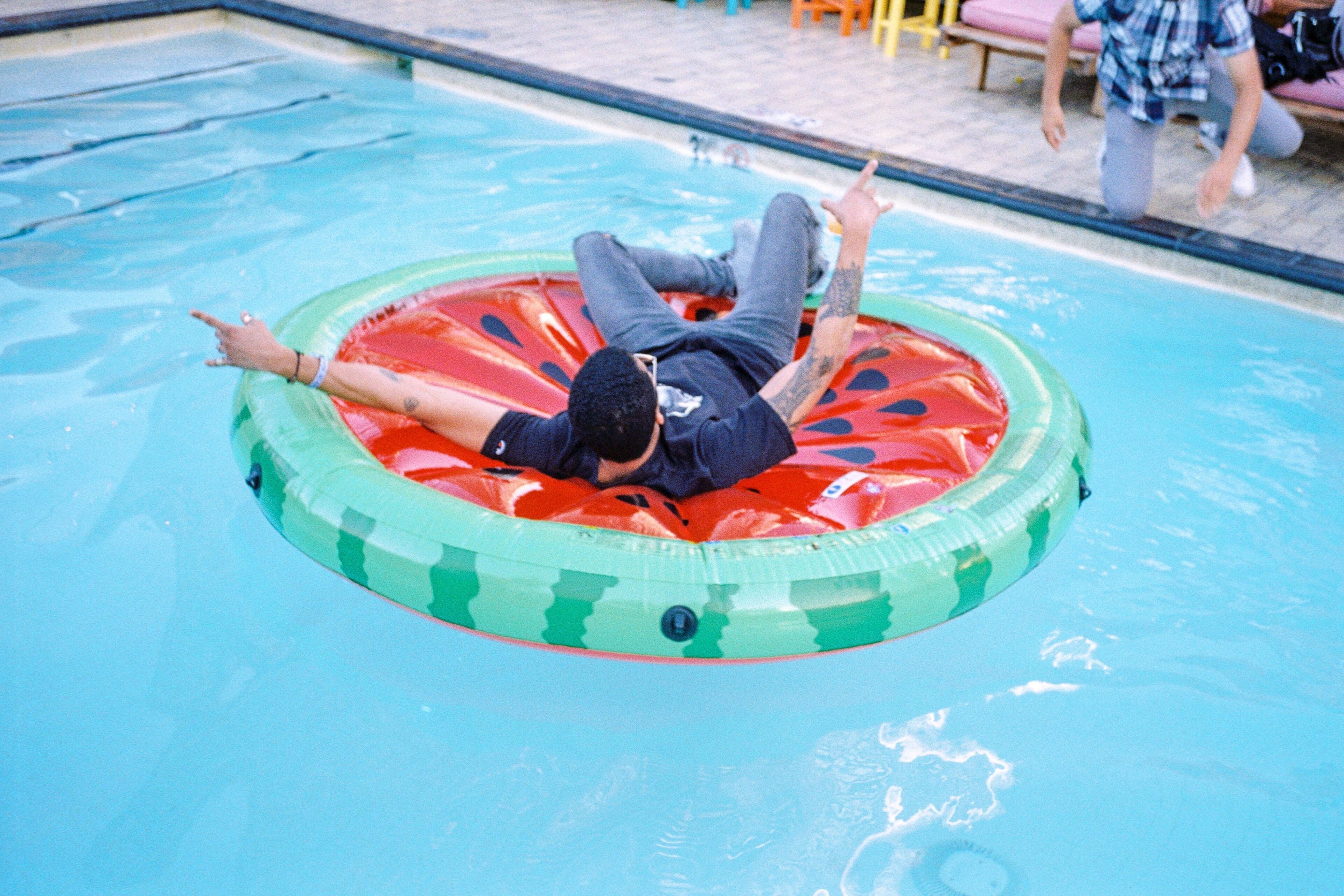 A person lying on a red and green inflatable ring in a swimming pool.