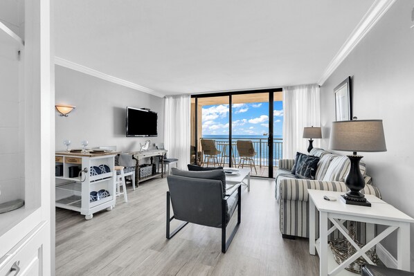 A modern hotel room with a balcony, a dining area, a sofa, and a TV.