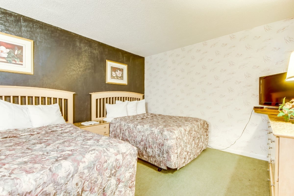 A hotel room with two beds, a desk with a lamp, a mirror, and a framed picture on the wall.