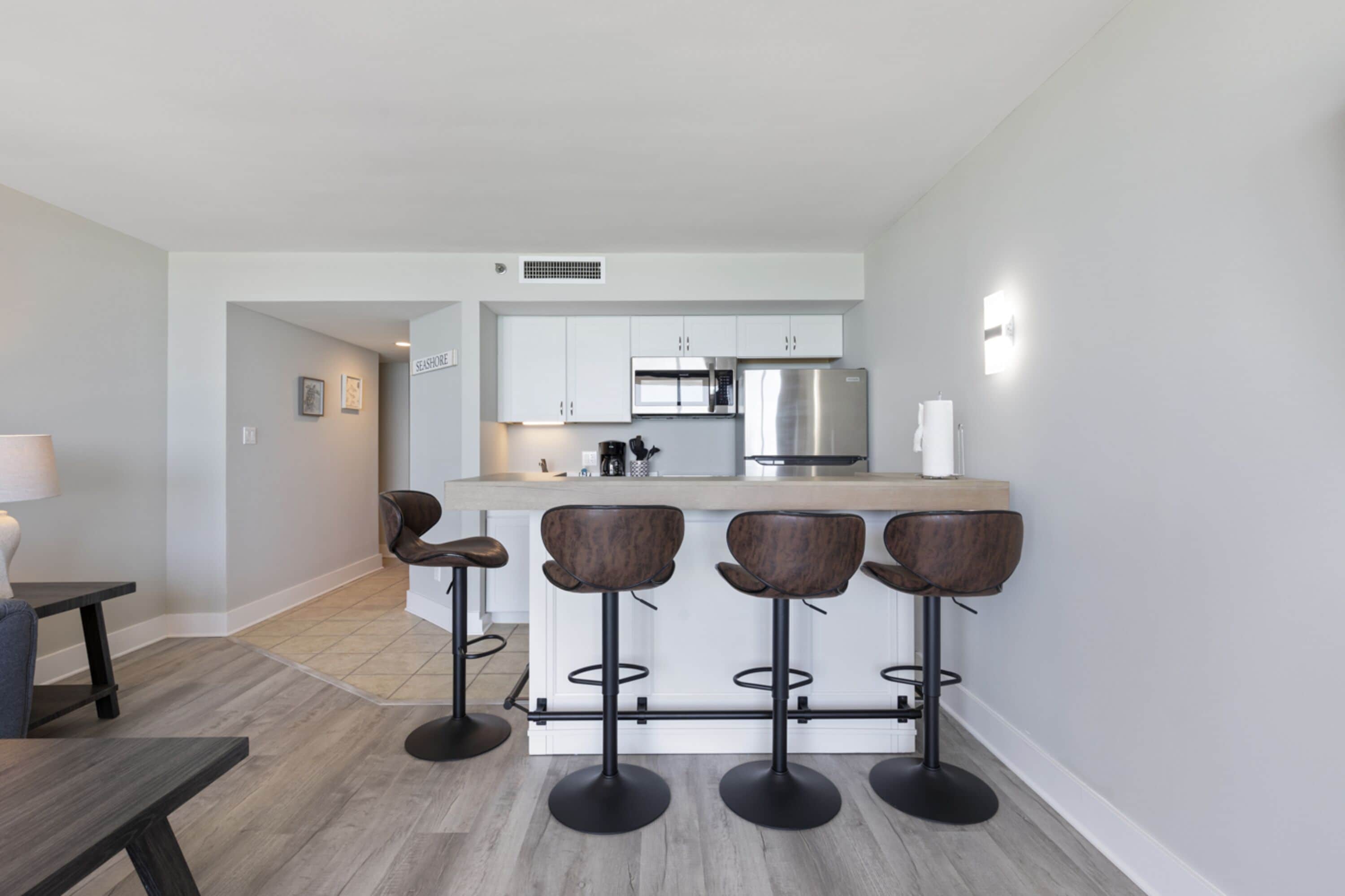 A modern kitchen with white cabinets, a stainless steel refrigerator, and a bar area with four stools.