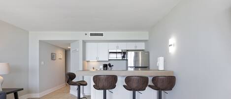 A modern kitchen with white cabinets, a stainless steel refrigerator, and a bar area with four stools.