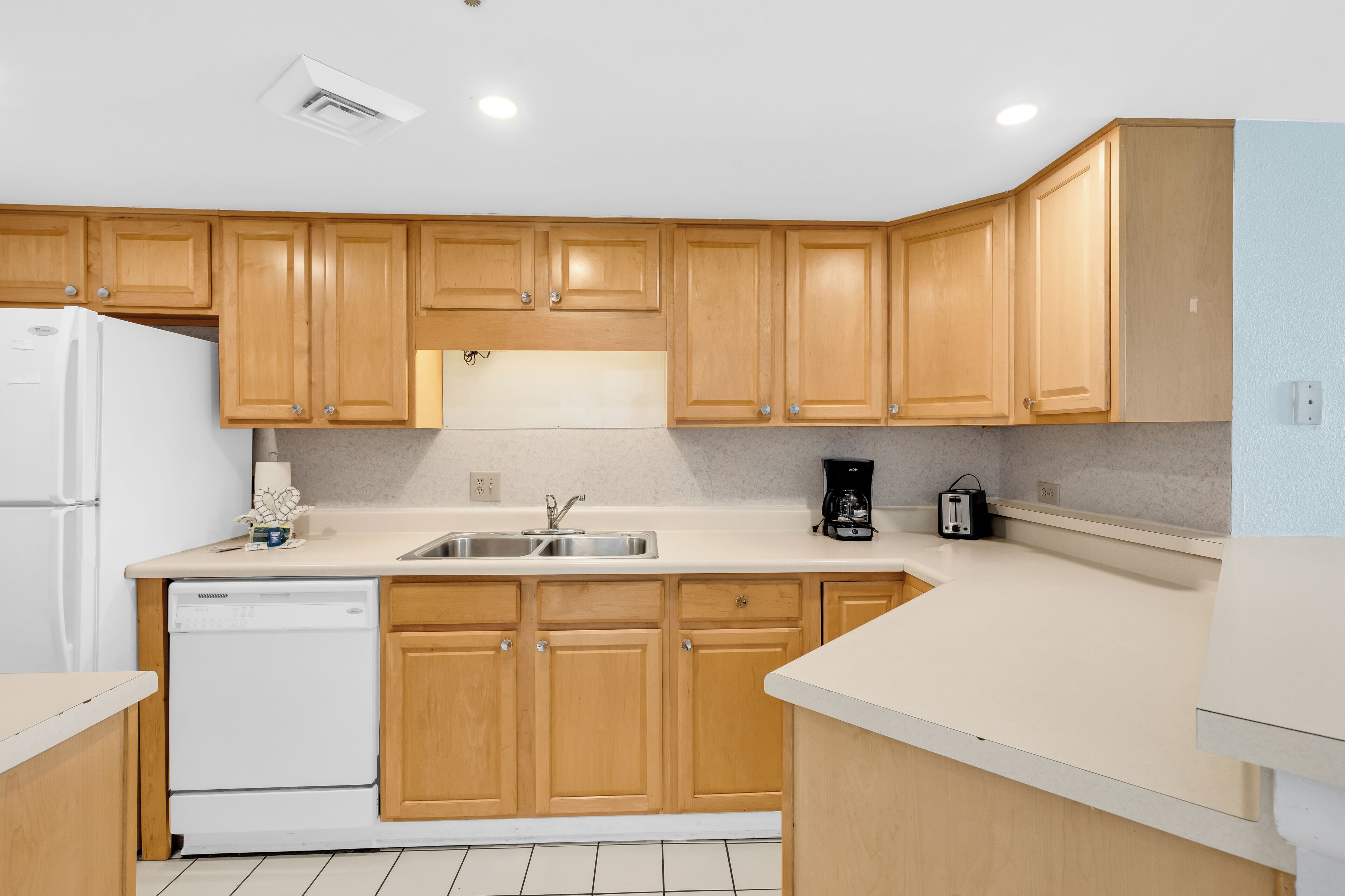 A kitchen with wooden cabinets, a white dishwasher, a sink, and a coffee maker.
