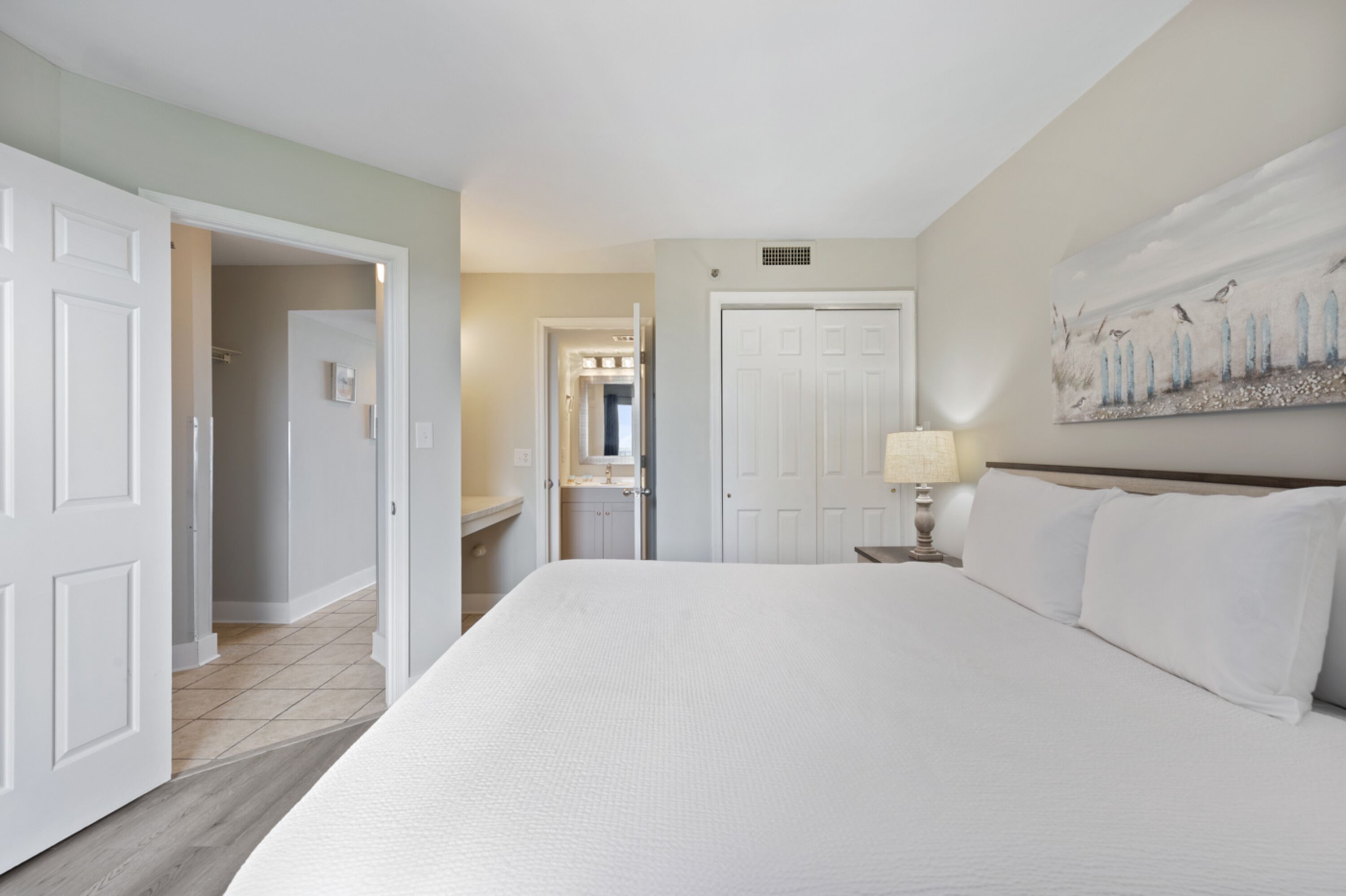 Une chambre d’hôtel avec un grand lit, une table de chevet avec une lampe, une porte donnant sur une salle de bain et un tableau au mur.