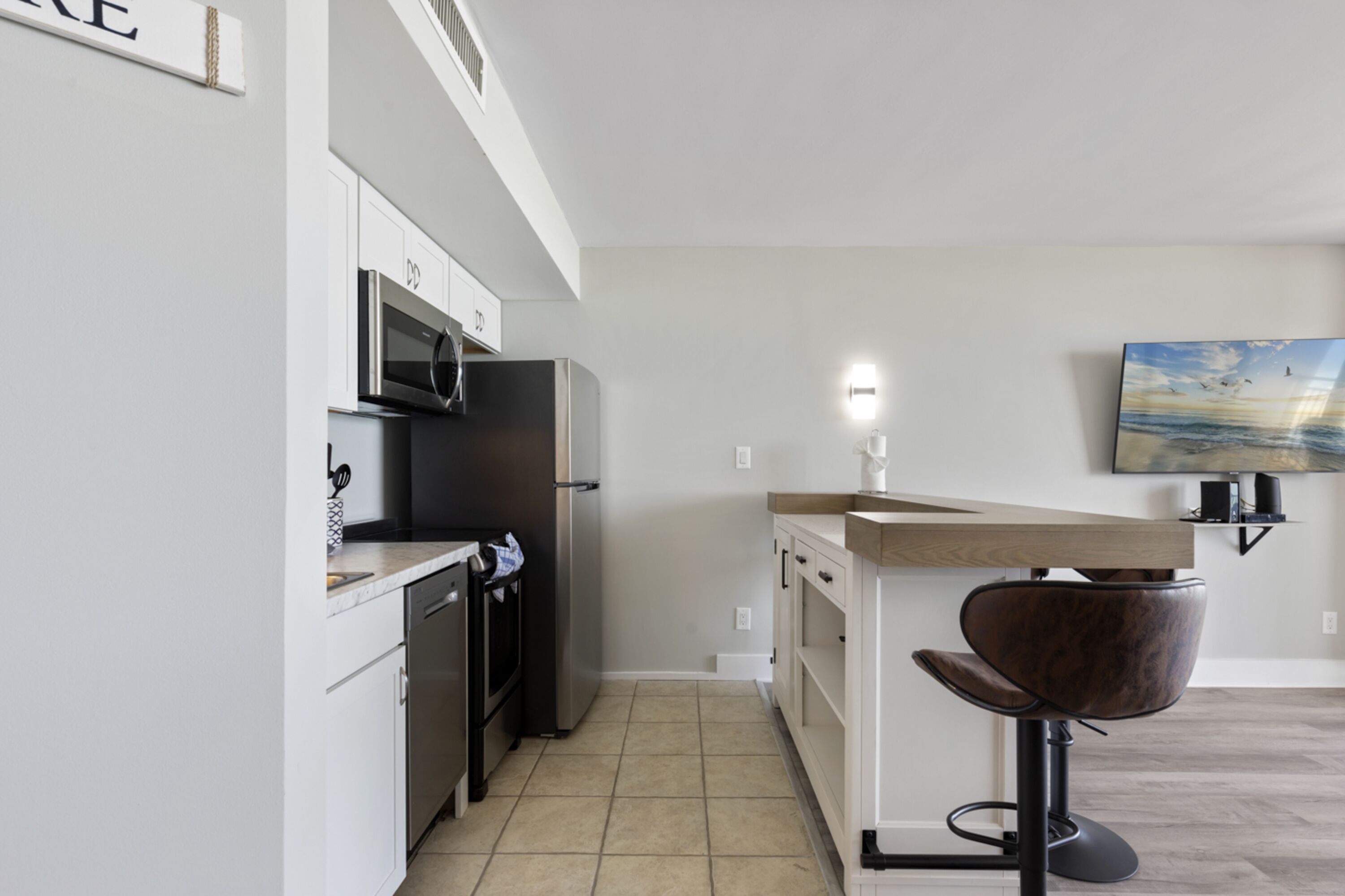 A modern kitchen with white cabinets, a microwave, a refrigerator, and a wooden countertop.