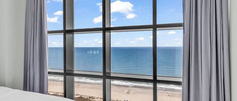 A room with a large window offering a view of a beach and ocean.