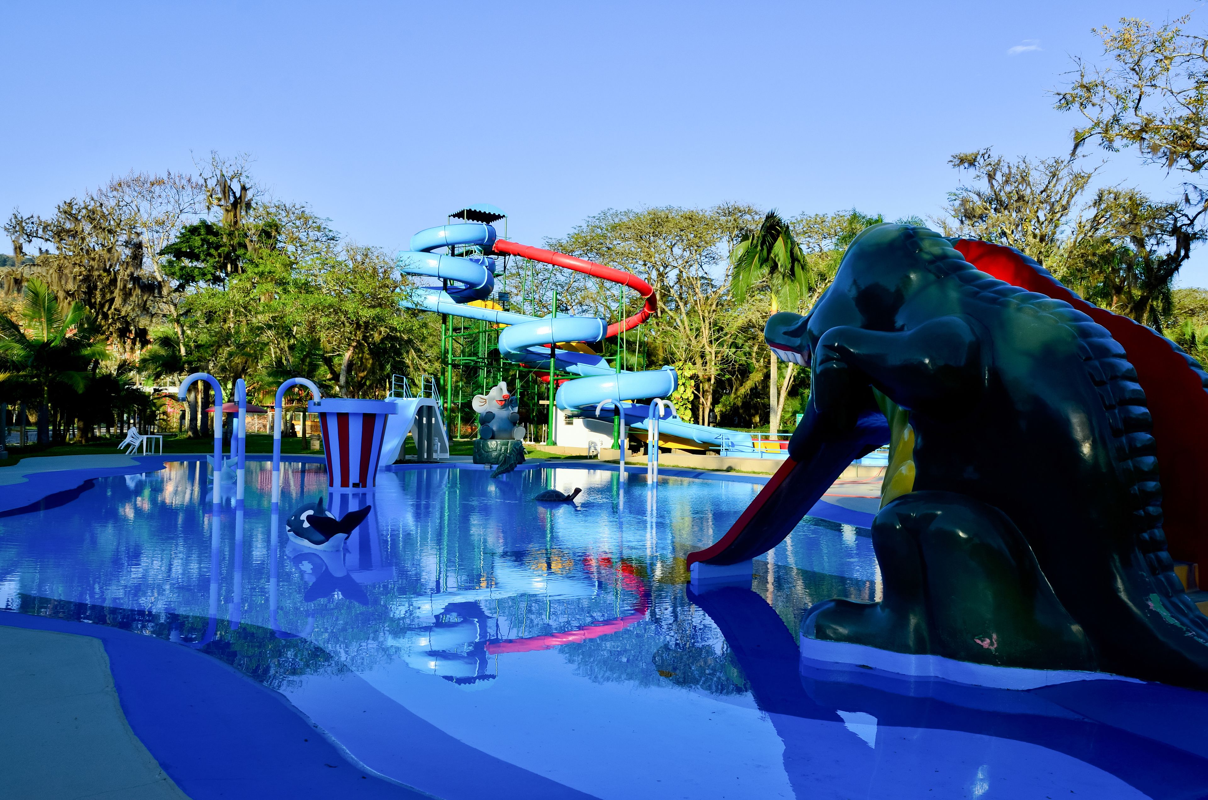 Parque acuático con una piscina grande, un tobogán de agua y una estatua de dinosaurio.