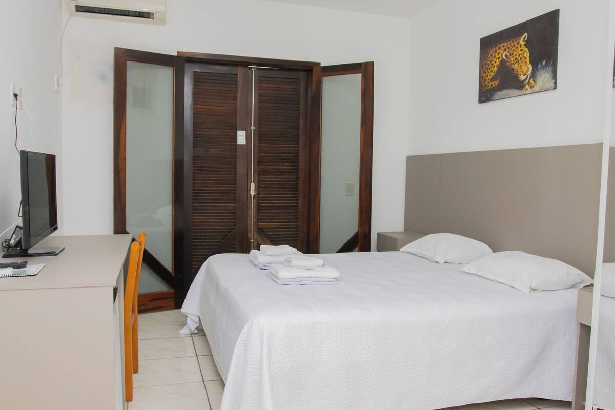 A bedroom with a bed, a desk with a computer, and a wardrobe.